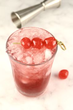 a red drink with ice and cherries on the rim, next to a pepper shaker