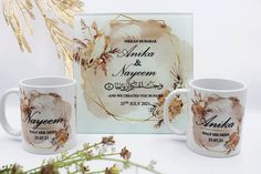 two coffee mugs sitting next to each other in front of a frame with flowers