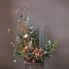 a christmas arrangement with candles and greenery in a vase on a wooden table next to a wall