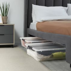 two plastic storage containers sitting on the floor in front of a bed with white pillows