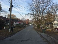 an empty street with houses in the background and power lines above it on either side