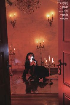 a woman sitting on the floor in front of a chandelier filled with candles