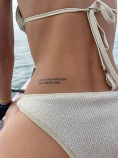 the back of a woman's body with a tattoo on her left side that reads,