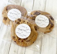 three chocolate chip cookies wrapped in plastic on top of a white wooden table with love is sweet stickers