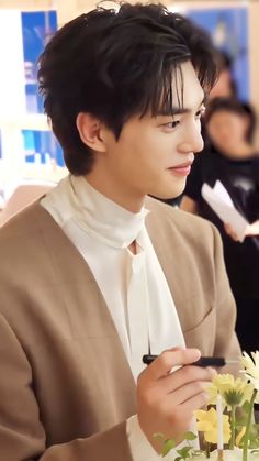 a young man in a suit and tie sitting at a table with flowers on it