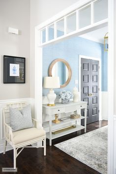 a living room with blue walls and white furniture in front of a mirror on the wall