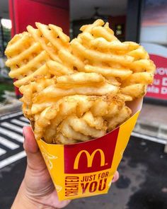 a person holding up a box of fries in front of a mcdonald's restaurant