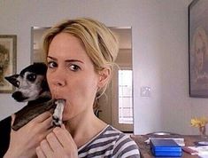 a woman holding a small dog in her lap while eating something out of the mouth