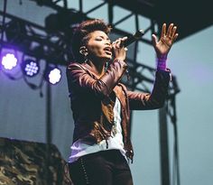 a woman standing on top of a stage with her hands up in the air as she sings