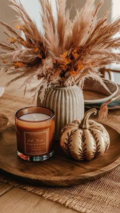 a candle sits on a wooden plate next to some pumpkins and pamodia