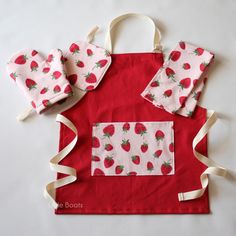 a red apron with strawberrys on it and two matching oven mitts