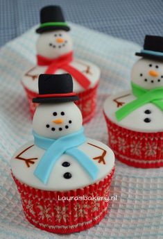 three cupcakes with frosting and snowmen on them sitting on a table