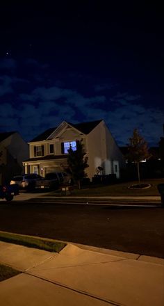 a street at night with cars parked on the side and houses in the back ground