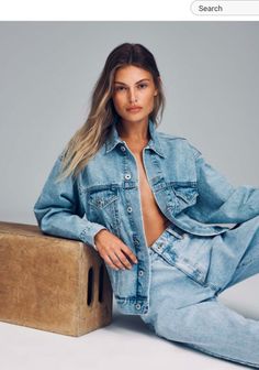 a woman sitting on top of a wooden block wearing jeans and a jean jacket with her hands in her pockets