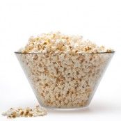 a glass bowl filled with popcorn next to a white background