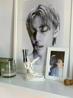 a white shelf topped with pictures next to a glass vase filled with water and a bird figurine