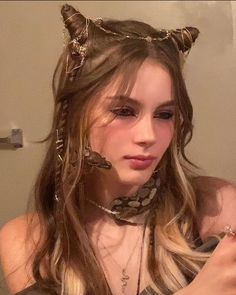 a woman with horns and chains on her head is brushing her hair in front of a mirror