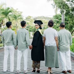 a group of people standing next to each other in front of trees and bushes with one woman wearing a graduation gown