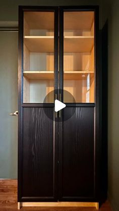 a wooden cabinet with glass doors in the middle of an empty room and wood flooring