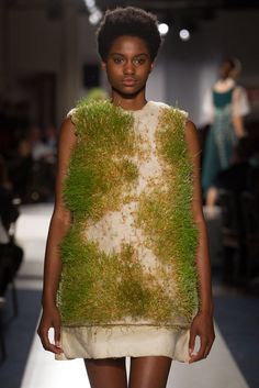 a model walks down the runway in a short dress with grass on it