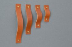 three pieces of orange leather with gold rivets on grey background, top view