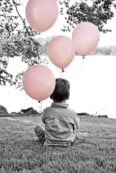 a little boy sitting in the grass with some balloons