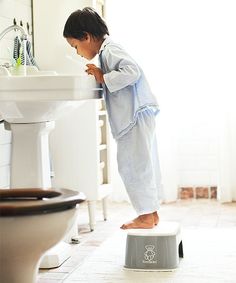 a little boy standing on top of a stool in front of a sink and toilet