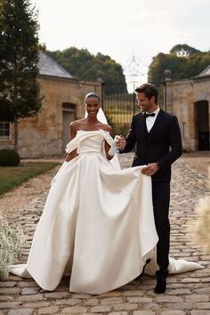 a man and woman in formal wear walking down a cobblestone road