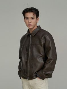 a young man wearing a brown leather jacket and white pants standing in front of a gray background