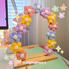 a crocheted wreath with flowers is on a table next to a computer monitor