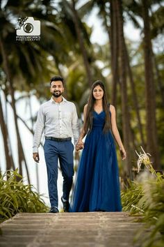 a man and woman holding hands while walking down a wooden walkway with palm trees in the background