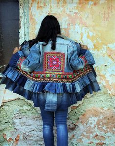 a woman standing in front of an old building wearing a denim jacket with colorful embroidered details