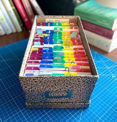 a box filled with lots of different colored pencils on top of a blue cutting mat