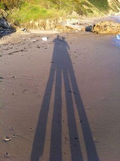 the shadow of two people standing on top of a sandy beach