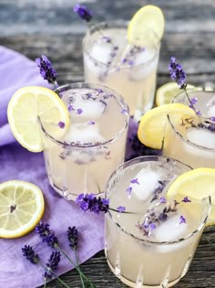 three glasses filled with lavender lemonade on top of a wooden table next to sliced lemons