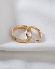 two gold wedding rings sitting on top of a white cloth