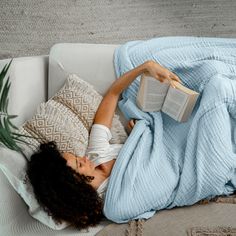 a woman laying on a couch reading a book