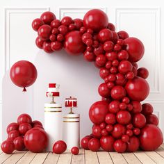 red balloons are arranged in the shape of an arch and two white cylinders with candles on them