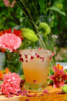 a glass filled with liquid sitting on top of a wooden table next to pink flowers