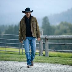 a man wearing a cowboy hat walking down a dirt road