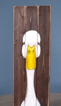 a white duck with a yellow beak standing in front of a wooden panel