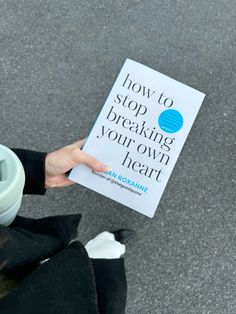 a person holding up a book about how to stop breaking your own heart on the street