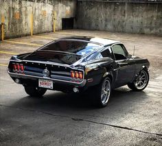 an old black car parked in a parking lot next to a concrete wall and cement floor