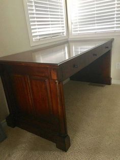 a wooden desk sitting in front of two windows with shutters on the outside side