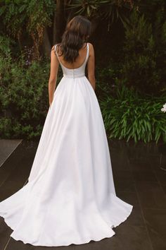 a woman in a white wedding dress is looking down at the ground with her back to the camera