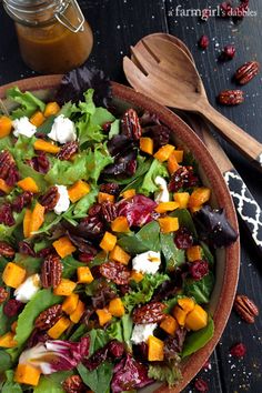 a salad in a bowl on a table next to a wooden spoon and some pecans