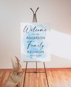 a welcome sign is on an easel in front of a white wall and wooden floor