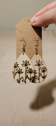 a pair of wooden earrings with black and white designs on them, being held by a hand