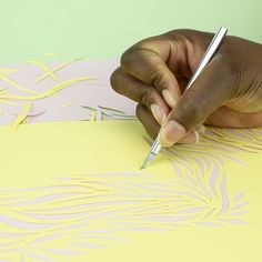 a hand holding a pen writing on a piece of paper with yellow and white designs