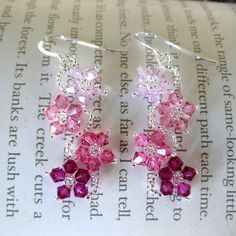 two pairs of pink and purple crystal earrings on top of a piece of paper next to an open book